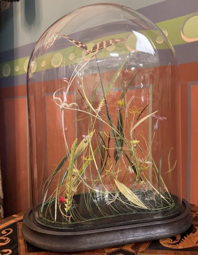 Summer Growth £2,900. Made from wire buttercups, daisies and speedwell with, velvet/feather grasses, iridescent flowers, feather moth and velvet caterpillar, in antique glass dome. Size: H 38cm W 30cm D 20cm. Sales: contact studio@bridgetbailey.co.uk